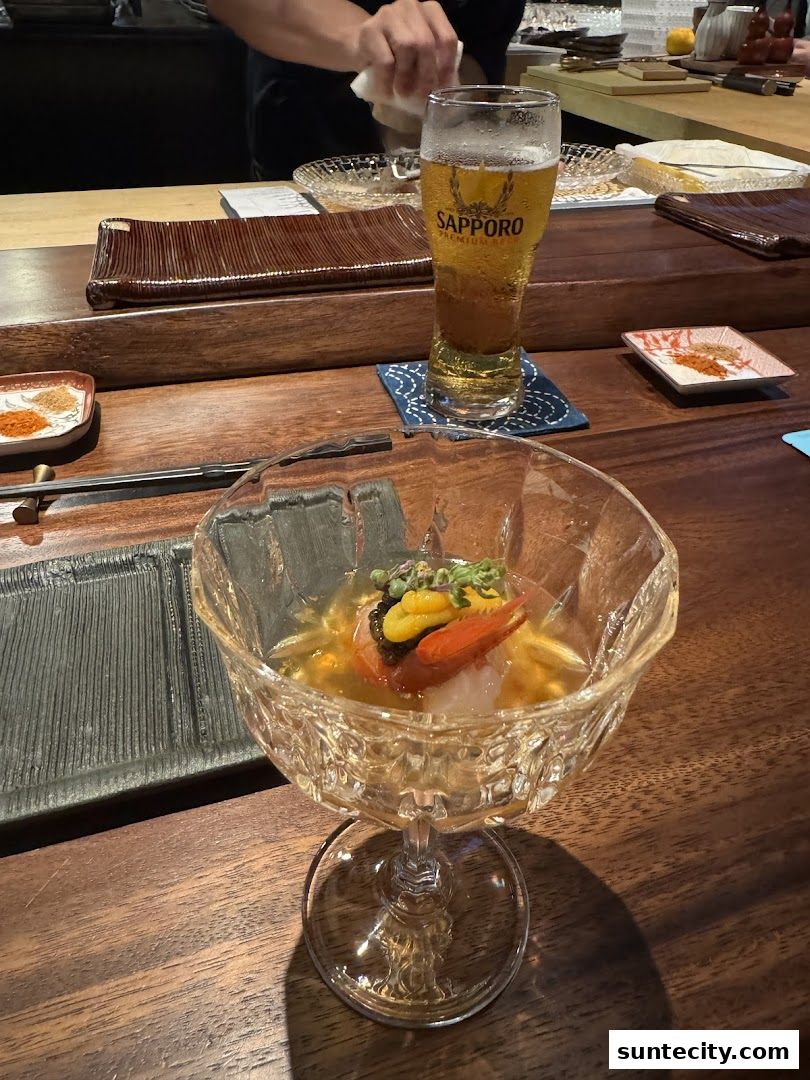 A glass of Sapporo beer and a delicate seafood appetizer served at a wooden counter.