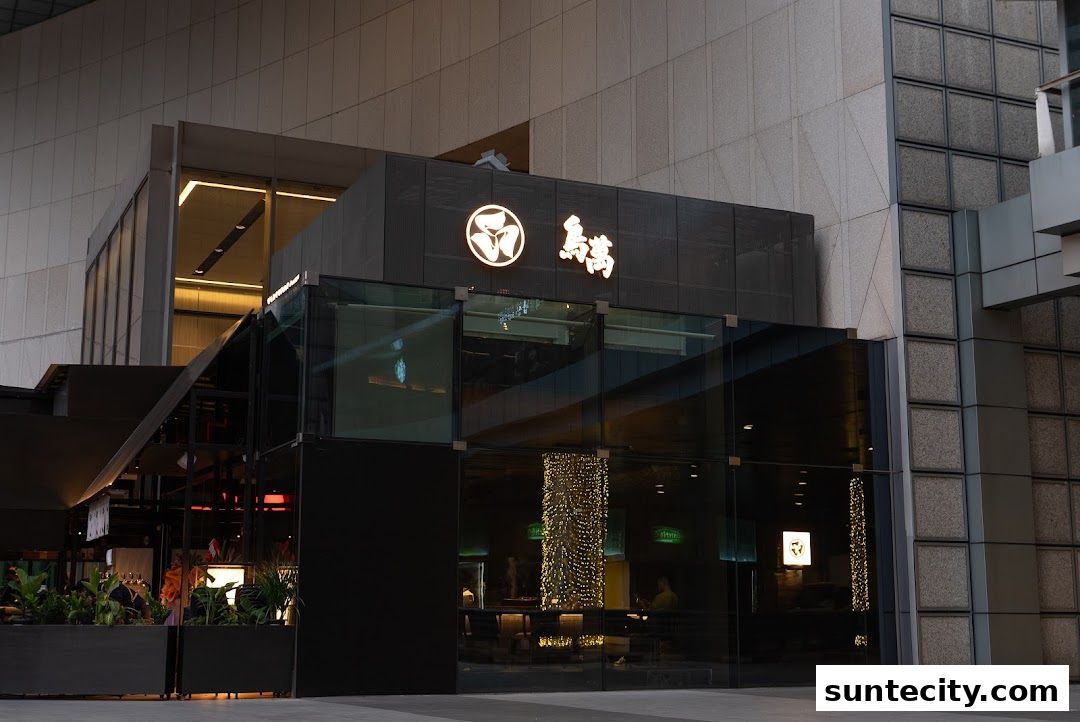 The modern storefront of Yakitori ONE 鳥萬 features a sleek black facade with large glass windows and illuminated signage.