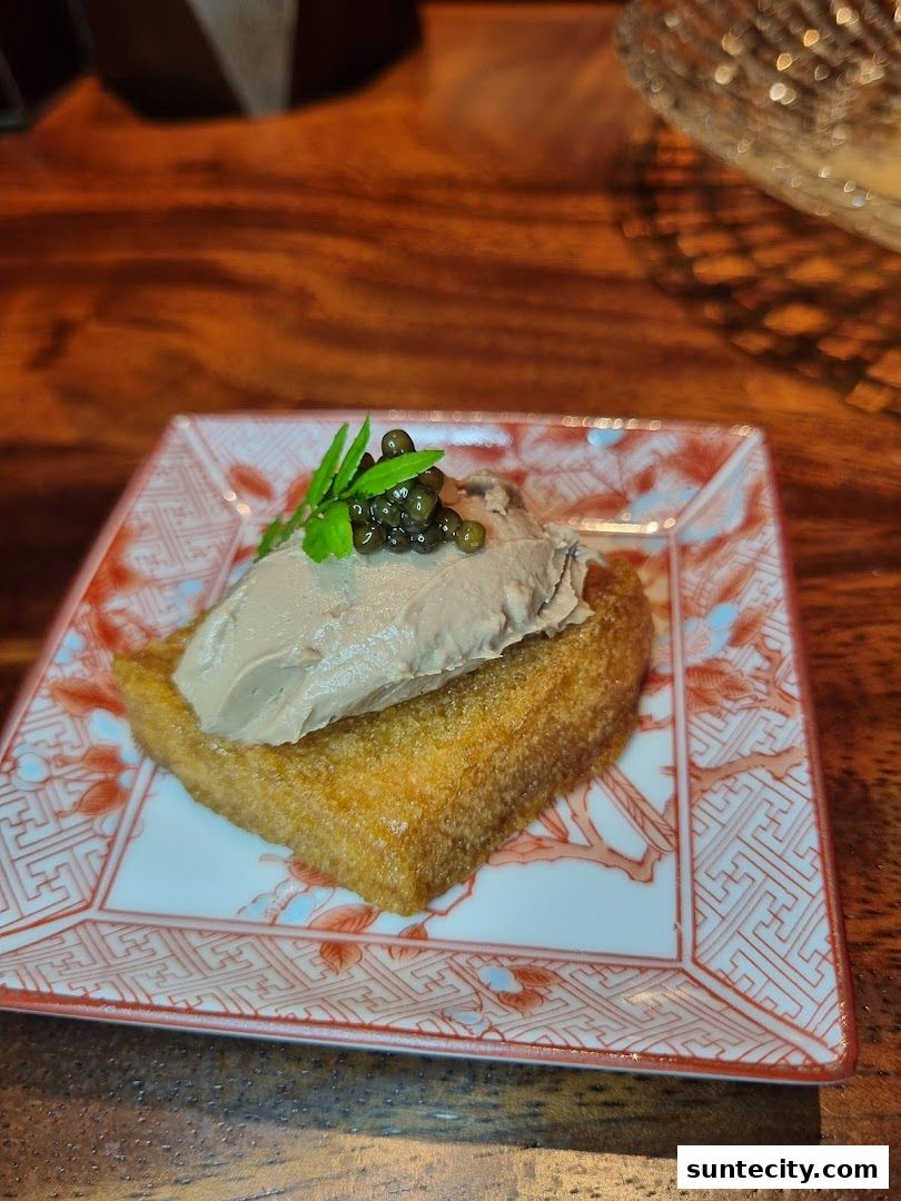 A close-up of a delicate appetizer with pâté, caviar, and garnish on a decorative plate.