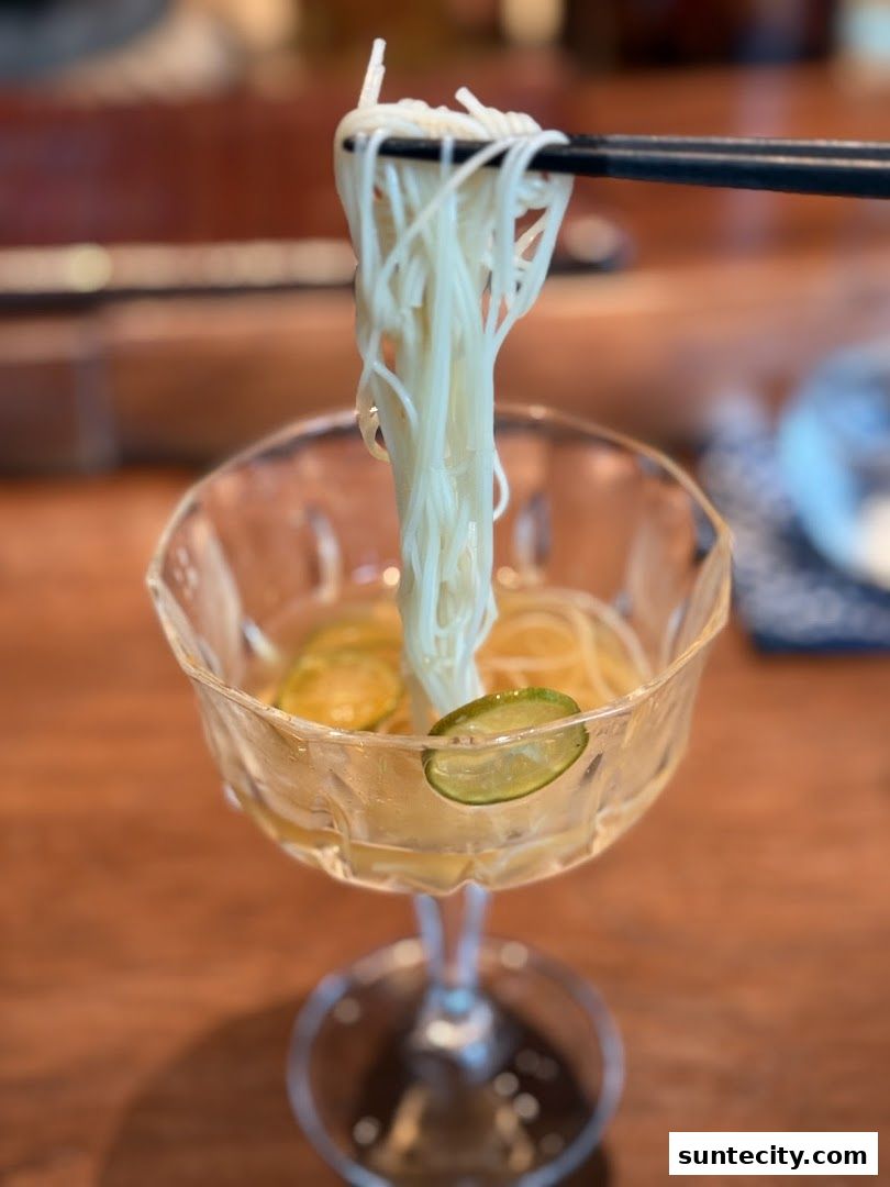 Chopsticks lift delicate white noodles from a glass bowl with citrus slices.