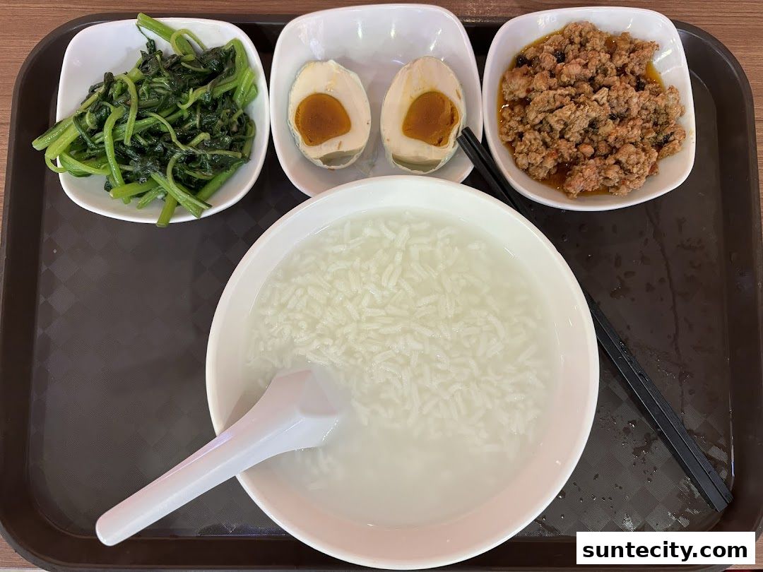 A tray of Teochew porridge with side dishes: stir-fried vegetables, salted egg, and minced meat.