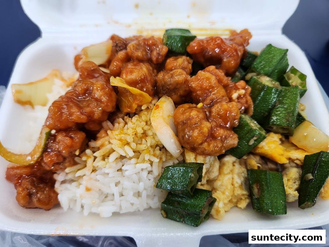 A close-up of a takeaway container filled with rice, sweet and sour chicken, okra, and scrambled eggs.