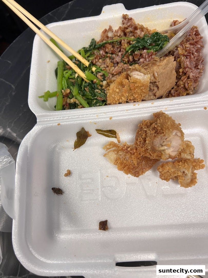 A takeout container with brown rice, vegetables, and fried chicken, with chopsticks.